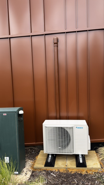 Daikin outdoor condenser unit on a timber base against copper cladding