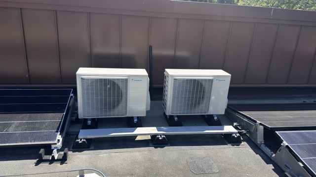 Two air conditioning condenser units on a flat roof beside solar panels