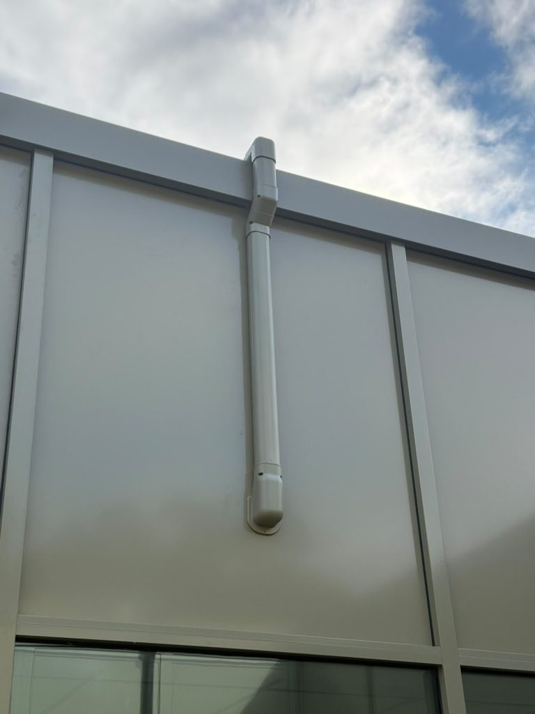Neat white pipe trunking running down a clad building exterior
